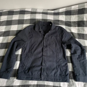 Mörkblå overshirt Lindberch  - Snygg mörkblå overshirt med klassisk krage och tre fickor framtill. Jackan har raka linjer, knäppning med stora knappar och är tillverkad i ett mjukt bomullstyg. Perfekt för lager-på-lager och enkel att styla till olika outfits.