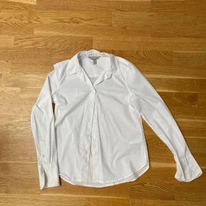 Vit klassisk skjorta - Säljer en stilren vit skjorta med krage och knappar framtill. Skjortan har lång ärm och en klassisk passform som funkar till många olika looks. Perfekt att styla med jeans eller kjol för en clean vibe.