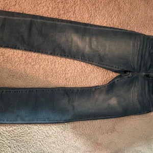 Blå jeansbyxor från AB Industries - Säljer ett par snygga blå jeansbyxor från AB Industries. De har en rak passform och är tillverkade i denim med snygga slitningar och kontrastsömmar. Perfekta för dig som har fresh/grish stil.