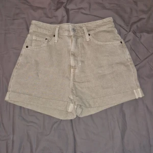 Beige shorts - Säljer ett par beige mom shorts från &Denim med ultra hög midja och regular fit. Klassisk femficksmodell i denim med uppvikta benslut och knappgylf. Perfekta för en avslappnad stil. Säljer pga icke använda😊
