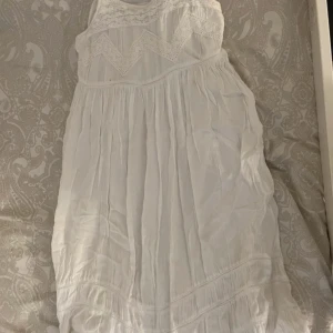Vit sommarklänning med spets från Happy Holly - Säljer en söt vit klänning från Happy Holly i storlek 32/34. Klänningen har spetsdetaljer upptill, volang nertill och är ärmlös. Perfekt för varma dagar och midsommarfirande!