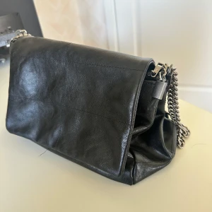 Svart väska från zara - Snygg svart axelväska i skinn med silverfärgad kedjerem från zara. Väskan har flera fack, varav ett med dragkedja, och stängs med magnetlås. Perfekt storlek för det viktigaste och passar till många olika stilar.