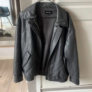 Grå grön quiltad skinnjacka från Meotine - Säljer en svart quiltad skinnjacka från Meotine i storlek S/M. Jackan har dragkedja, krage och ribbade muddar vid ärmslut och nederkant. Snygg och stilren modell som passar till många outfits. Köpt för 1500