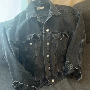 Svart jeansjacka från Perfect Jeans - Klassisk svart jeansjacka från Perfect Jeans i storlek M. Jackan är mer som en oversize look. Jackan har silverfärgade knappar framtill och på bröstfickorna, samt klassisk krage och sömdetaljer. Jackan är i jeans material. Lite tjockare material. Perfekt för vår och sommar. Köpt förra våren. Använts 1 gång 
