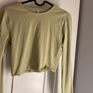 Ljusgrön croppad långärmad topp från NLY Trend - Säljer en ljusgrön croppad långärmad topp från NLY Trend. Enkel och stilren design med rund halsringning och smal passform. Knytning runt mage. Perfekt att matcha med jeans eller kjol för en trendig look.
