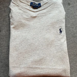 Grå tröja från Polo Ralph Lauren -  Säljer en klassisk grå tröja från Polo Ralph Lauren med liten broderad logga på bröstet. Tröjan är tillverkad i 100% bomull och har en enkel, stilren design med rund hals. Perfekt för en avslappnad och snygg look.