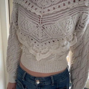 Vit stickad croppad tröja med spetsdetaljer - Säljer en vit stickad croppad tröja med vackra spetsdetaljer och mönsterstickning. Tröjan har lång ärm och bred ribbad mudd i midjan. 
