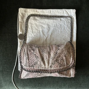 Äkta Stella McCartney väska - Axelväska från Stella McCartney i ormmönster med kedjedetaljer i silver. Väskan har en mjuk, slouchy form och en bred axelrem i metall. Väskan är äkta och dustbag tillkommer 💕