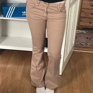 Beiga lågmidjade bootcut jeans - Säljer ett par beiga bootcut jeans med klassisk femficksdesign och låg midja. Byxorna har dragkedja och knapp framtill och är tillverkade i ett mjukt bomullsmaterial med lite stretch. De är oanvända! 