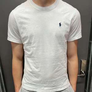 Ralph Lauren t shirt - Klassisk vit t-shirt från Ralph Lauren med liten blå broderad logga på bröstet. T-shirten har rund halsringning och korta ärmar. Perfekt basic-plagg för garderoben. Storlek L men passar M