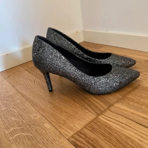 Glittriga pumps från Catwalk - Säljer ett par snygga pumps från Catwalk i silverglittrigt material. Skorna har spetsig tå och smal klack, perfekta för att sticka ut på festen. Klassisk modell med bekväm passform och elegant look.