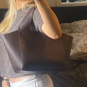 Brun carin wester väska - Säljer denna snygga Carin Wester väskan! Den är köpt på Åhlens hemsida för 399kr, den heter ”Liten toteväska SANYA” på Åhlens hemsida.🌻 Den är i helt nyskick, aldrig använd. ☕️🍂😽🙌🏼🍸  Lite info: • Liten toteväska i polyuretan🍸 • Breda axelremmar😽 • Magnetknapp i toppen🙌🏼 • Fästen för fodral ur serien MIX💋  Mått på väskan: Bredd nedtill: 30 cm🦭 Bredd upptill: 50 cm🍂 Höjd: 26 cm🥀 Djup: 14 cm🌞 Dropplängd: 18 cm🪐  - väskan har invändiga remmar med fästen ☕️ 