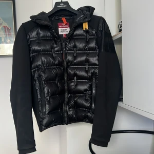 ÄKTA Svart cardigan  från Parajumpers - Säljer en svart pufferjacka från Parajumpers med huva och dragkedja. Jackan är köpt på Johnells. Kvitto och lappar finnns. Bara att höra av er om frågor. Tar även byten. Ny pris 7000kr 