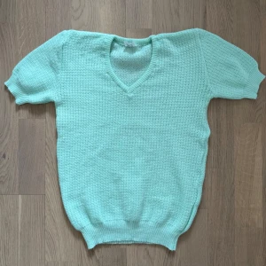 Vintage Mintgrön stickad tröja med v-ringning - Säljer en mintgrön stickad tröja i 100% akryl med v-ringad hals och korta ärmar. Tröjan har en luftig och mjuk känsla, perfekt för lager-på-lager. Tillverkad i Italien.