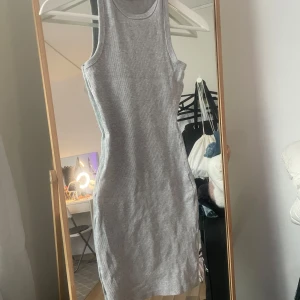 Grå ribbad klänning från F2 Sister - Säljer en grå, tight ribbad klänning från F2 Sister. Klänningen är ärmlös med sportig racerback och har en kroppsnära passform. Perfekt för en enkel och stilren look. Materialet är mjukt och stretchigt för extra komfort.