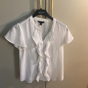 Vit blus med volang från Banana Republic - Säljer en stilren vit blus från Banana Republic i storlek XS. Jätte söt nu inför sommaren och den är i oanvänt skick! 