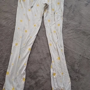 Blommiga pyjamasbyxor med snörning - Säljer ett par bekväma pykamasbyxor i ljus färg med gulligt blommönster i gult. Byxorna har en elastisk midja med snörning för justerbar passform. Perfekta för en avslappnad dag hemma. Har ett litet hål på höger ficka