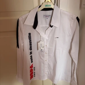 Vit skjorta från U.S. Polo Assn. - Snygg vit skjorta från U.S. Polo Assn. med svarta detaljer och texttryck på framsidan. Skjortan har en klassisk krage och knappar framtill. Perfekt för en stilren look. (aldrig använt)