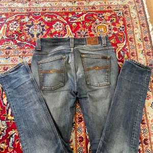 Nudie jeans ”grim trim” - Säljer ett par snygga blå jeans med passformen grimtim (slimfit) från Nudie Jeans med slitna detaljer och klassisk femficksdesign. är tillverkade i högkvalitativt denim. Hål i båda fickorna men går enkelt att fixa.