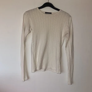 Brandy Melville - Säljer en stilren vit ribbad tröja från Brandy Melville. Tröjan har långa ärmar och en enkel design som passar perfekt till olika outfits. Perfekt för en avslappnad look.