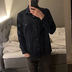 J.Lindberg, overshirt - Säljer en stilren overshirt i hög kvalitet! Den är gjord av mjukt och behagligt tyg som gör den perfekt för både vardag och fest. Overshirten har en klassisk krage och knäppning fram, vilket ger den en tidlös look. 