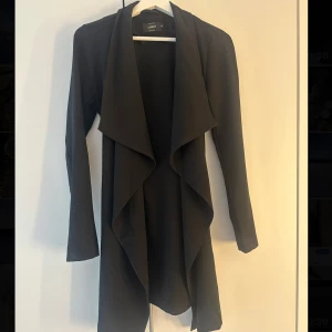 Svart tunnare kappa från Only - Snygg svart tunnare kappa från Only med långa ärmar och en elegant draperad design framtill, och en rosett man kan knyta baktill. Storlek: Xs men passar även mig som har S🩷🫶🏼