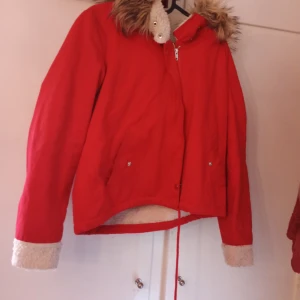 Röd jacka med fuskpäls - Snygg röd jacka med dragkedja och fuskpälsdetaljer på kragen och ärmsluten. Perfekt för kyliga dagar med sin varma och mysiga design.