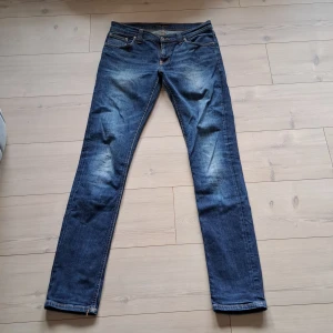 Blå jeans från Nudie Jeans - Snygga blå jeans från Nudie Jeans med klassisk femficksdesign och orange sömmar. De har en gylf och en bekväm passform som passar perfekt till vardags. Märkeslogga på bakfickan ger en extra touch.