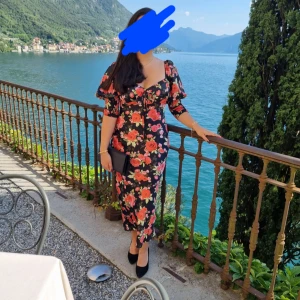 Blommig klänning med volangdetaljer - Säljer en vacker blommig klänning med volangdetaljer. Klänningen har en smickrande v-ringning och korta ärmar. Klänningen är i satin och använd 1 gång på ett bröllop i Italien. 