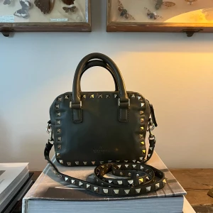 Grön handväska med nitar från Valentino - Snygg grön handväska från Valentino med coola nitar runt kanterna. Väskan har en avtagbar axelrem och två handtag för olika bärstilar. Modellen och färgen går inte att köpa längre ❤️