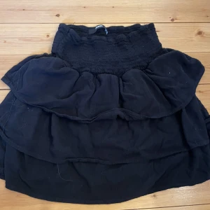 Svart volangkjol  - Snygg svart kortkjol med flera lager av volanger. Kjolen har en elastisk midja för bekväm passform. Perfekt för att styla med en enkel topp eller blus.