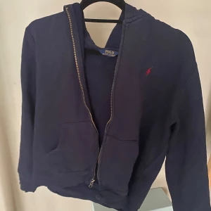 Mörkblå zip hoodie från Ralph Lauren - Säljer en snygg mörkblå zip hoodie från Ralph lauren. Bra för sommarn med denna blå färgen. Denna tröjan passar bäst för längderna 150-155 cm. Ny pris ca 1000 kr. Mitt pris 249kr.