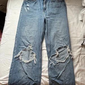 Blå jeans med slitningar - Säljer ett par blå jeans med coola slitningar på knäna. De har en klassisk femficksdesign och är avklippta där nere (köpta så). Använda ett fåtal gånger! Packar i plastpåse.
