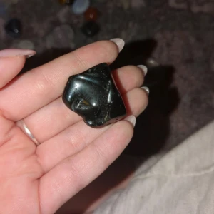 Svart Obsidian  - En svart, polerad sten med en slät yta och oregelbunden form. Perfekt som dekorativt inslag eller för samlingar.