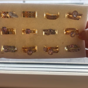 Samling av glittriga ringar i guld och silver - En vacker samling av ringar i både guld och silver. Ringarna har glittriga detaljer och flera av dem är prydda med stora, gnistrande stenar. Perfekt för att lägga till lite extra glamour till din stil.