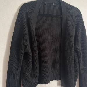Svart stickad kofta - Säljer en stilren svart stickad kofta med långärmad design. Perfekt för kyligare dagar och enkel att matcha med olika outfits. Koftan har en öppen front och ribbade detaljer som ger en klassisk look.