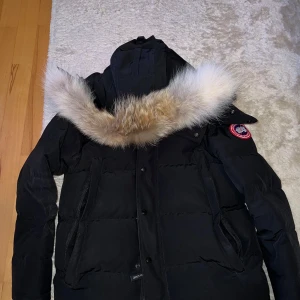 Svart Canada Goose Wyndham Parka - Svart Canada Goose Wyndham Parka säljs. Jackan har använts två vintrar men har tagits väl hand om. Jackan har även päls på luvan som går att ta bort (se de olika bilderna). Storleken på jackan är S. Jackan är köpt på NK en gång i tiden, men dessvärre finns inget kvitto kvar längre. Bara att skriva för fler frågor eller bilder. Priset kan INTE diskuteras.