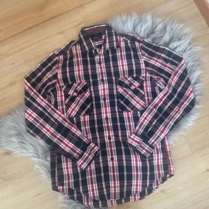 Rutig skjorta från GANT - Snygg rutig skjorta från GANT i marinblått, rött och vitt. Skjortan har långa ärmar och knappar framtill samt två bröstfickor med knappstängning. Perfekt för en stilren look.