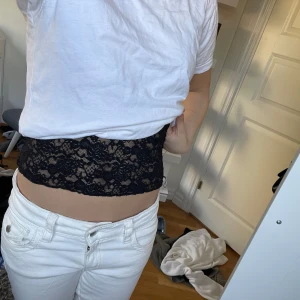 Svart spetslinne - Säljer ett svart spetslinne med v-ringad design och breda axelband. Perfekt för en stilren och elegant look. Passar bra till både jeans och kjol.