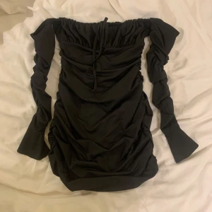 Svart offshoulder klänning med långa ärmar  - Snygg svart offshoulder klänning med långa ärmar och knytning framtill. Perfekt för en kväll ute eller en speciell tillställning. 