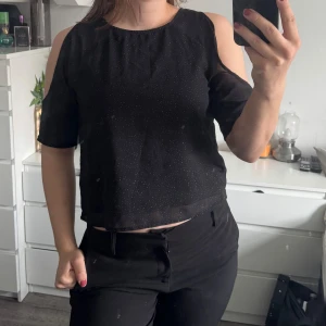 Svart glittrande blus - Snygg svart topp med glittrande detaljer. Toppen har en unik design med öppna axlar och korta ärmar. (Katt och kanin finns i hemmet) 