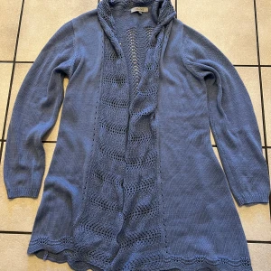 Blå stickad kofta från Cellbes storlek 42/44 - Snygg blå stickad kofta från Cellbes med dekorativa stickade detaljer längs framkanten. Perfekt för att hålla sig varm och stilren under kyligare dagar. Koftan har långa ärmar och en öppen design som gör den lätt att matcha med olika outfits.