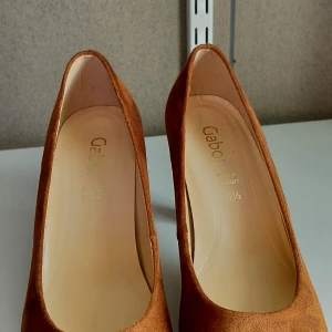Bruna mockapumps från Gabor - Snygga bruna pumps i mocka från Gabor med en elegant klack. Perfekta för att ge en stilren touch till din outfit. Skorna har en rund tå och är i storlek 6 1/2.