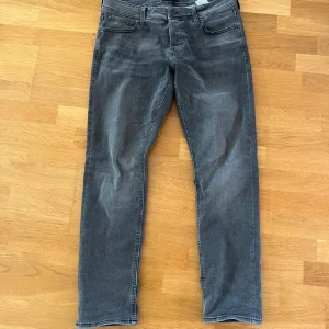 Grå jeans från Jack & Jones - Snygga grå jeans från Jack & Jones med en klassisk femficksdesign. De har en normal passform och är tillverkade i ett slitstarkt denimtyg. Perfekta för en avslappnad stil.