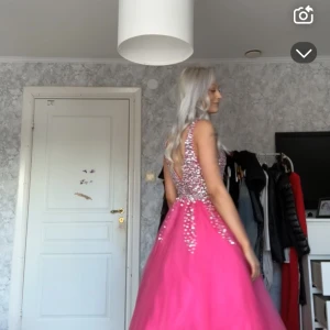 Rosa balklänning  - Säljer en fantastisk rosa balklänning med v-ringad design och öppen rygg. Klänningen är dekorerad med glittrande pärlor på överdelen och har en voluminös kjol. Perfekt för speciella tillfällen! 