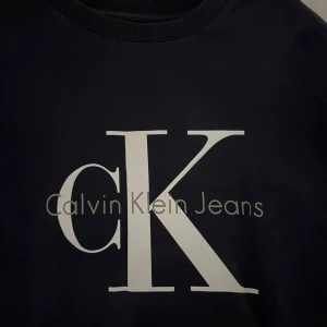 Mörk blå från Calvin Klein Jeans - Säljer en stilren mörk blå tröja från Calvin Klein Jeans med det ikoniska CK-logotypen tryckt på framsidan. Tröjan har långa ärmar och en klassisk rund halsringning. Perfekt för en avslappnad och trendig look. Andvänd få par gånger. Köpte för 1000 kr men säljer nu för 400 kr