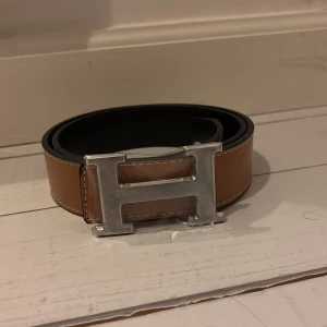 Brunt bälte med silverfärgat  H-spänne - Snyggt brunt bälte med ett stort silverfärgat H-format spänne. Tillverkat i skinn och perfekt för att ge en stilren touch till din outfit.