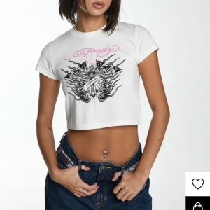 Vit croppad t-shirt från Ed Hardy - Snygg vit croppad t-shirt från Ed Hardy med ett coolt tryck i svart och rosa. Använd en gång i utmärkt skick köpt på Nelly.