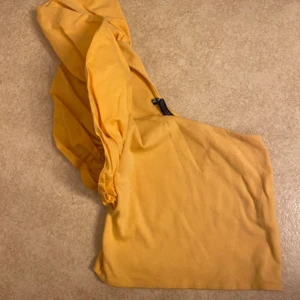 Gul oneshoulder topp - Säljer en snygg orange oneshoulder topp med en unik design. Toppen har en smickrande passform och är perfekt för att sticka ut. Den är tillverkad i ett mjukt material som känns skönt mot huden. Perfekt för sommarens alla tillfällen! 🌞