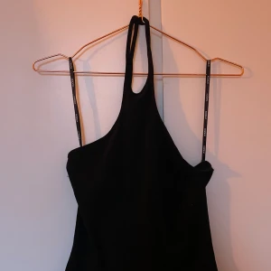 Svart halterneck topp från Kookai - Snygg svart halterneck topp från Kookai med smala axelband och stilren design. Perfekt för en chic och elegant look. Tillverkad i ett mjukt och bekvämt material.